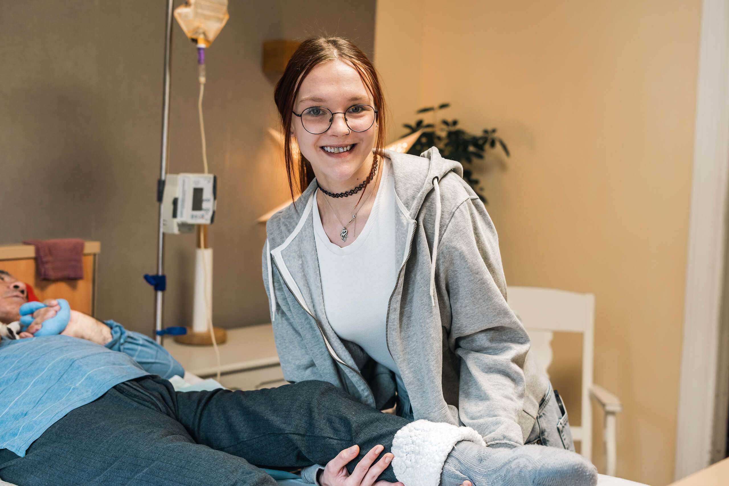 Junge Frau lächelt und hilft einem Patienten im Krankenhausbett mit einem Verband am Bein.
